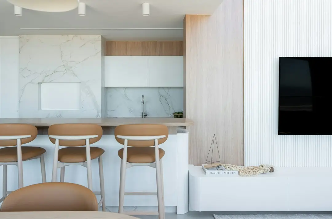 A modern open-plan room with a large wall-mounted TV next to a marble kitchen, the kind of screen for Nartiel8k 4K IPTV