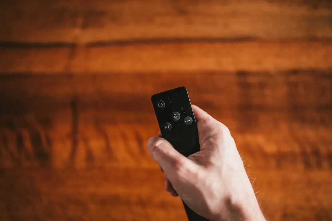 A hand holding a small streaming-device remote in front of a wooden wall, ready to set up IPTV Smarters with a Nartiel8k login